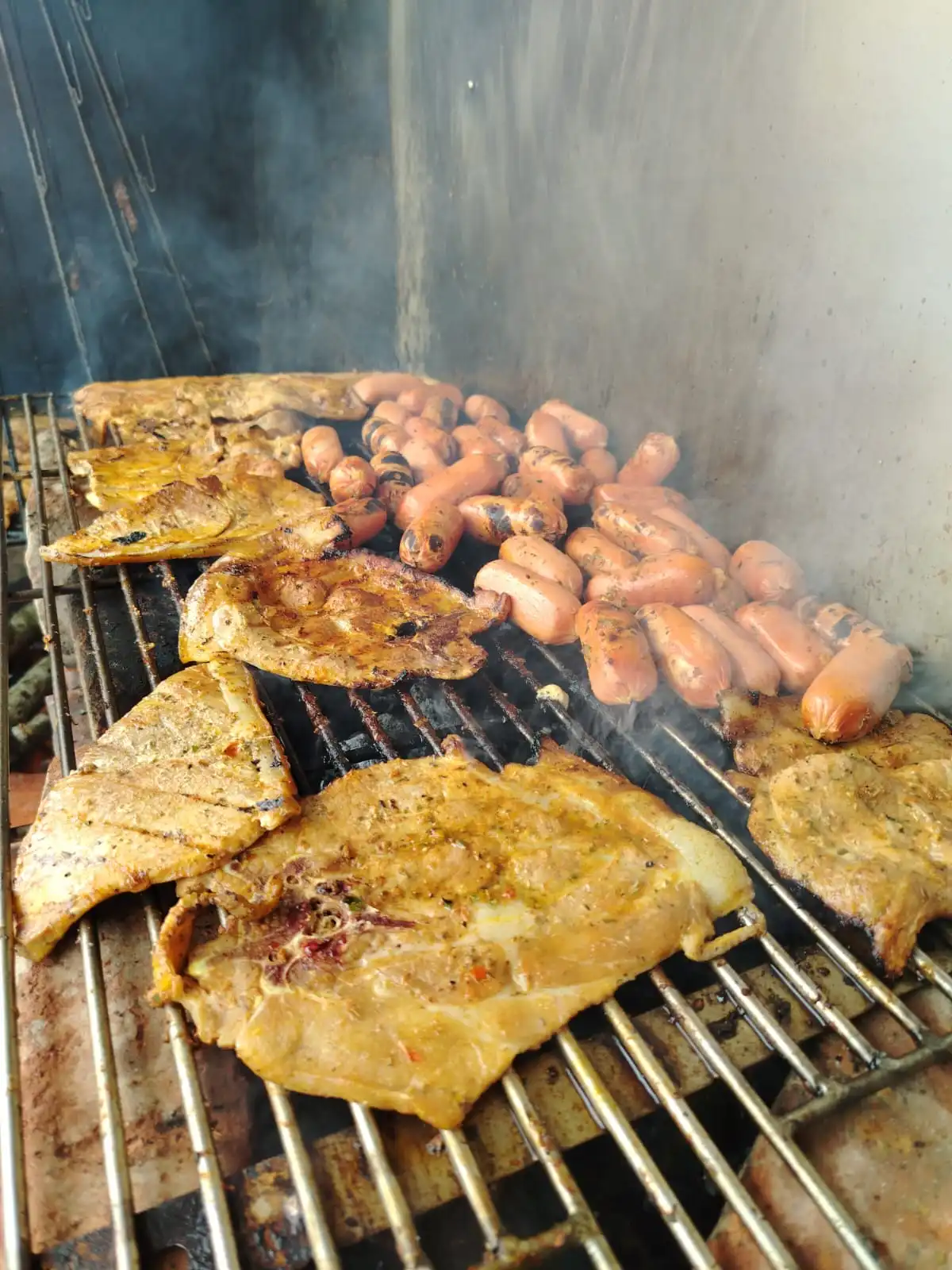 Parrilla con cortes y embutidos artesanales asándose a fuego vivo